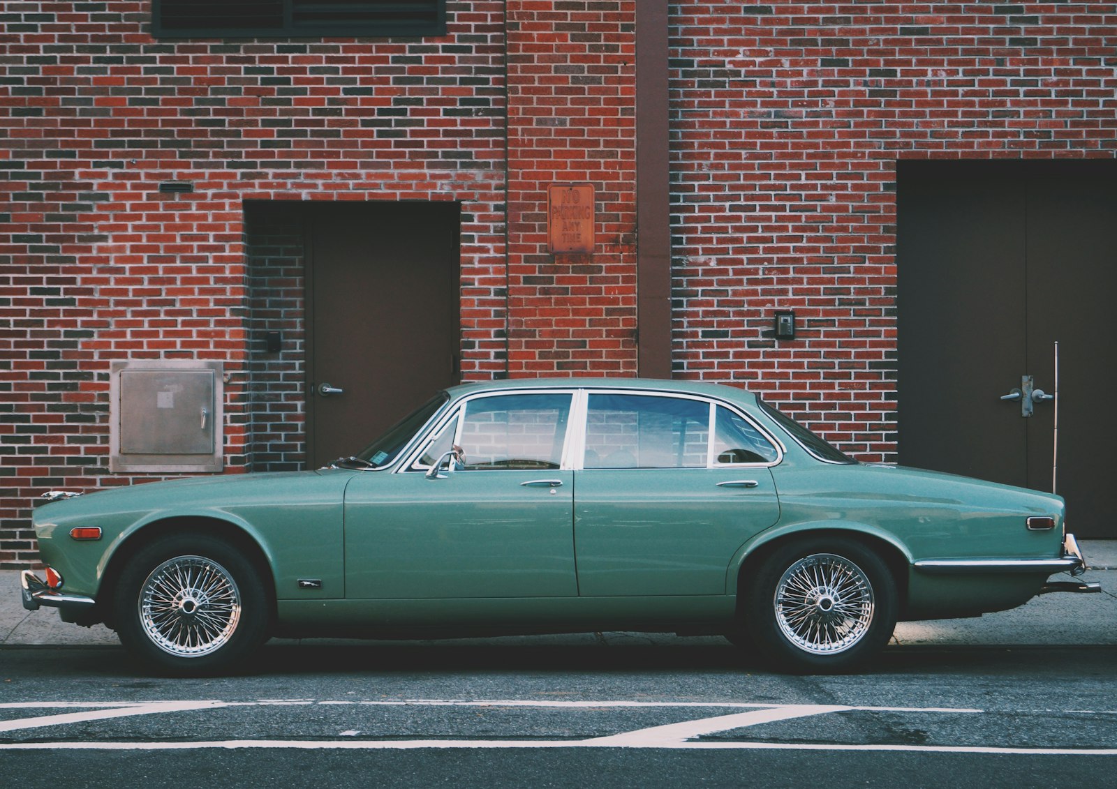 A teal classic sedan parked near a brick building